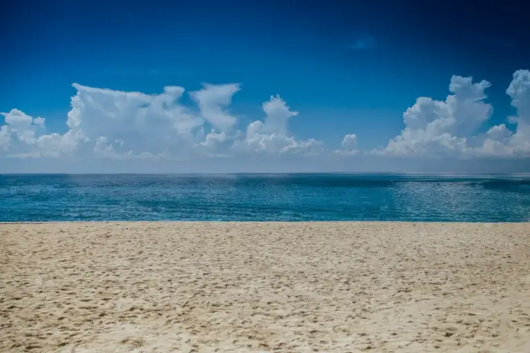 Wide sandy beach with blue ocean and cloudy sky.