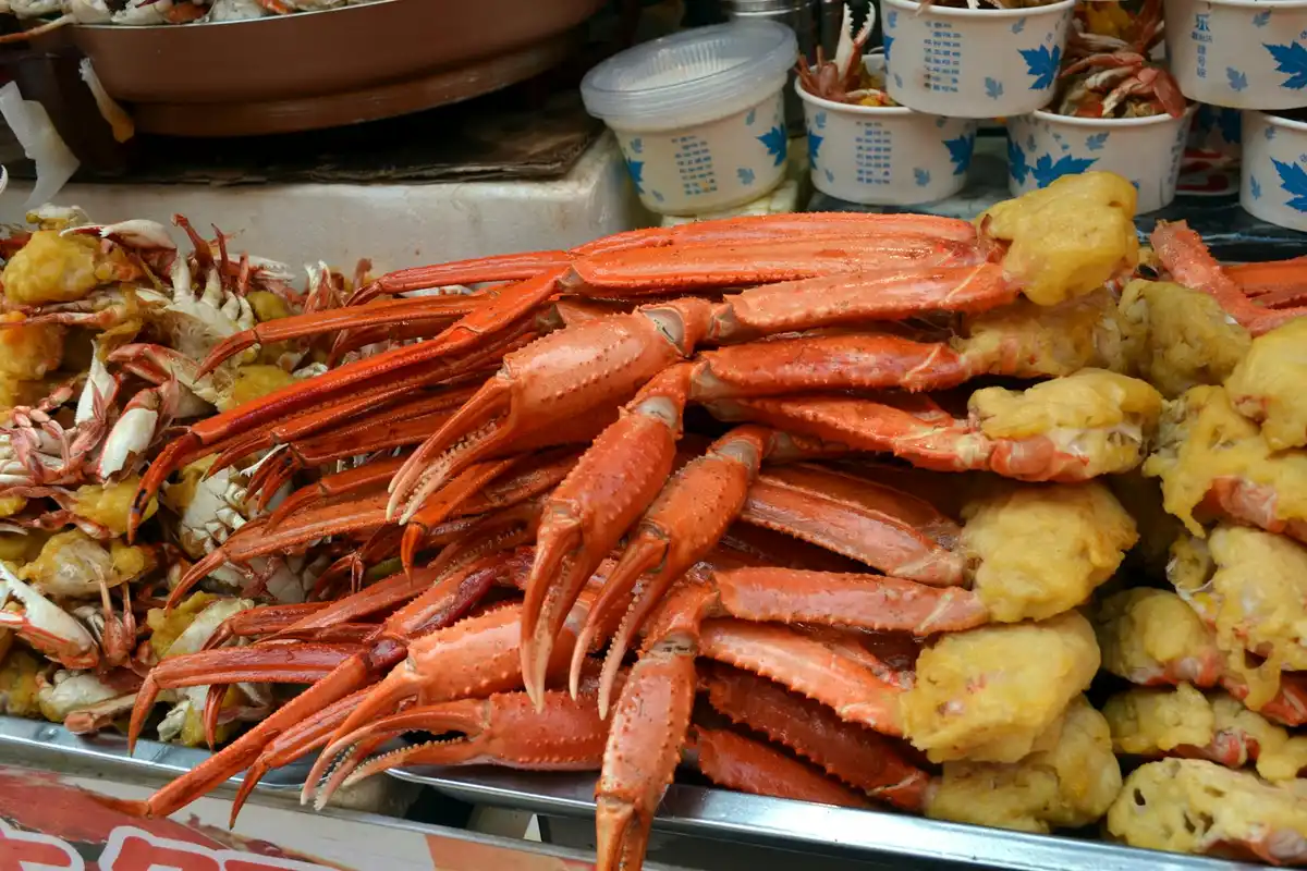 Red crustaceans piled on a market display with yellow fried snacks in the background.