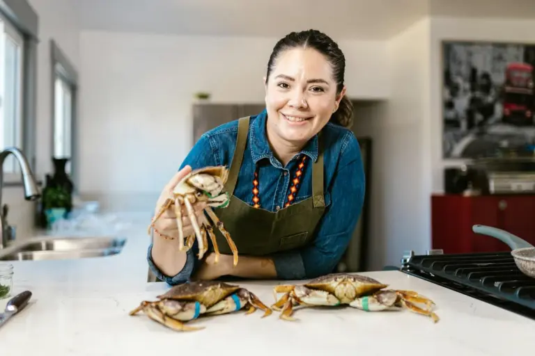 A person in a blue shirt and apron holds a large hermit crab while several hermit crabs sit on a white kitchen counter.