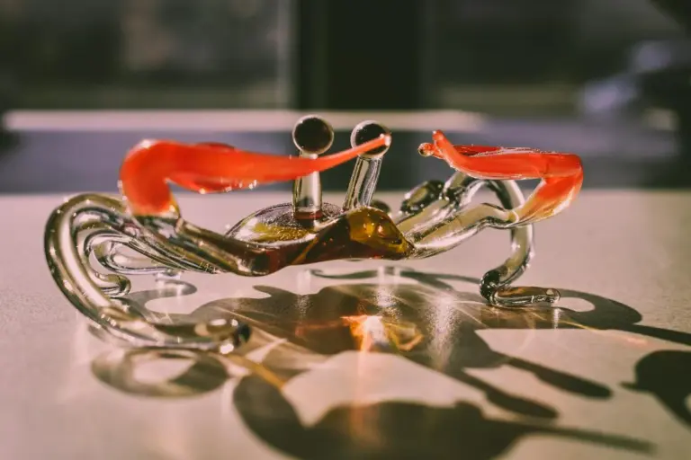 Close-up of a translucent glass hermit crab with bright orange claws on a reflective surface.