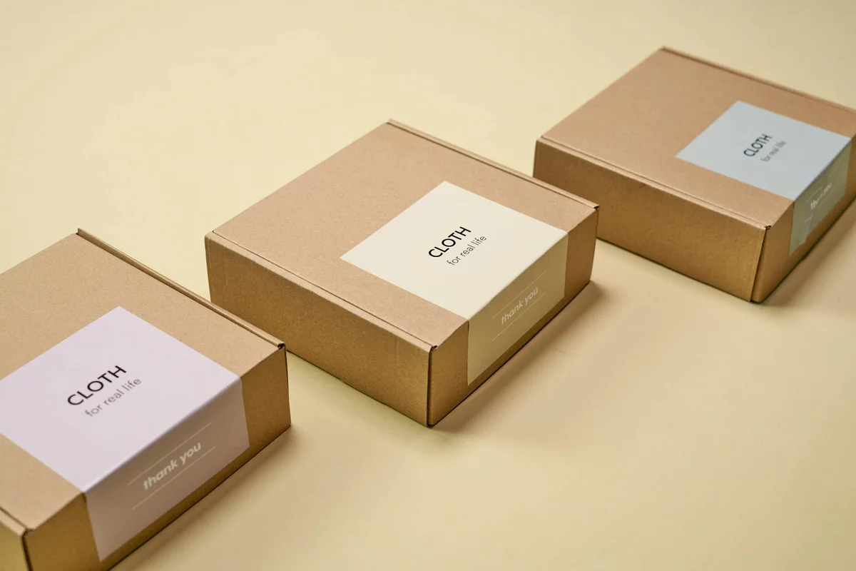 Three brown cardboard boxes with white labels that read 'CLOTH' arranged on a pale yellow surface.