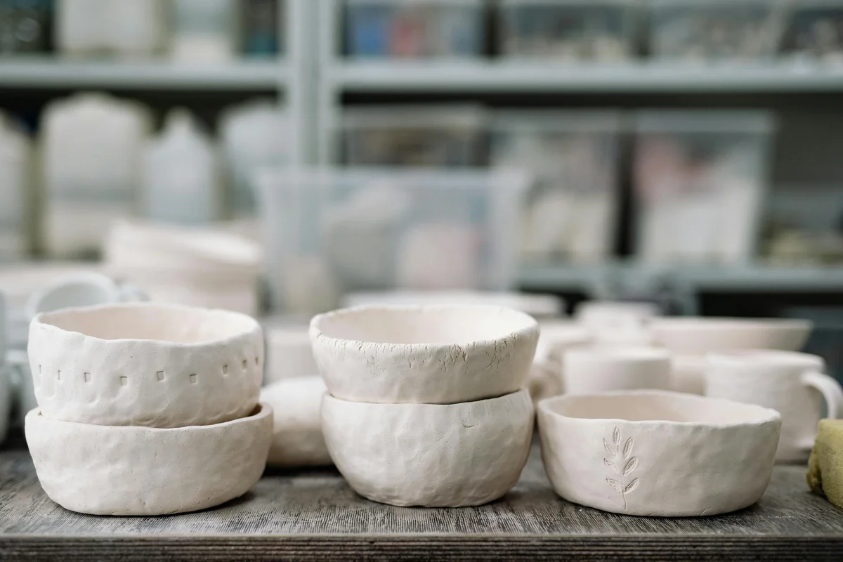 Several white ceramic bowls arranged on a wooden surface, prepared as food and water dishes for a hermit crab feeding station.
