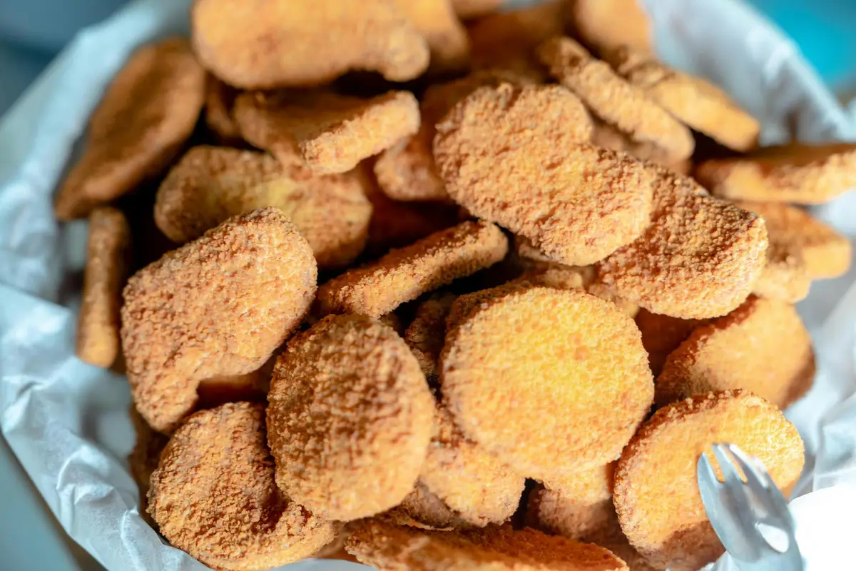 Close-up of a pile of round, orange-brown breaded pellets on a light surface, with a small fork visible.