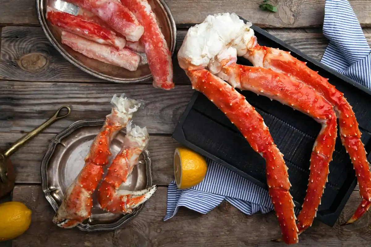 Crab legs and shell fragments on a rustic wooden table with a lemon and blue cloth, illustrating food preparation for hermit crab diets.