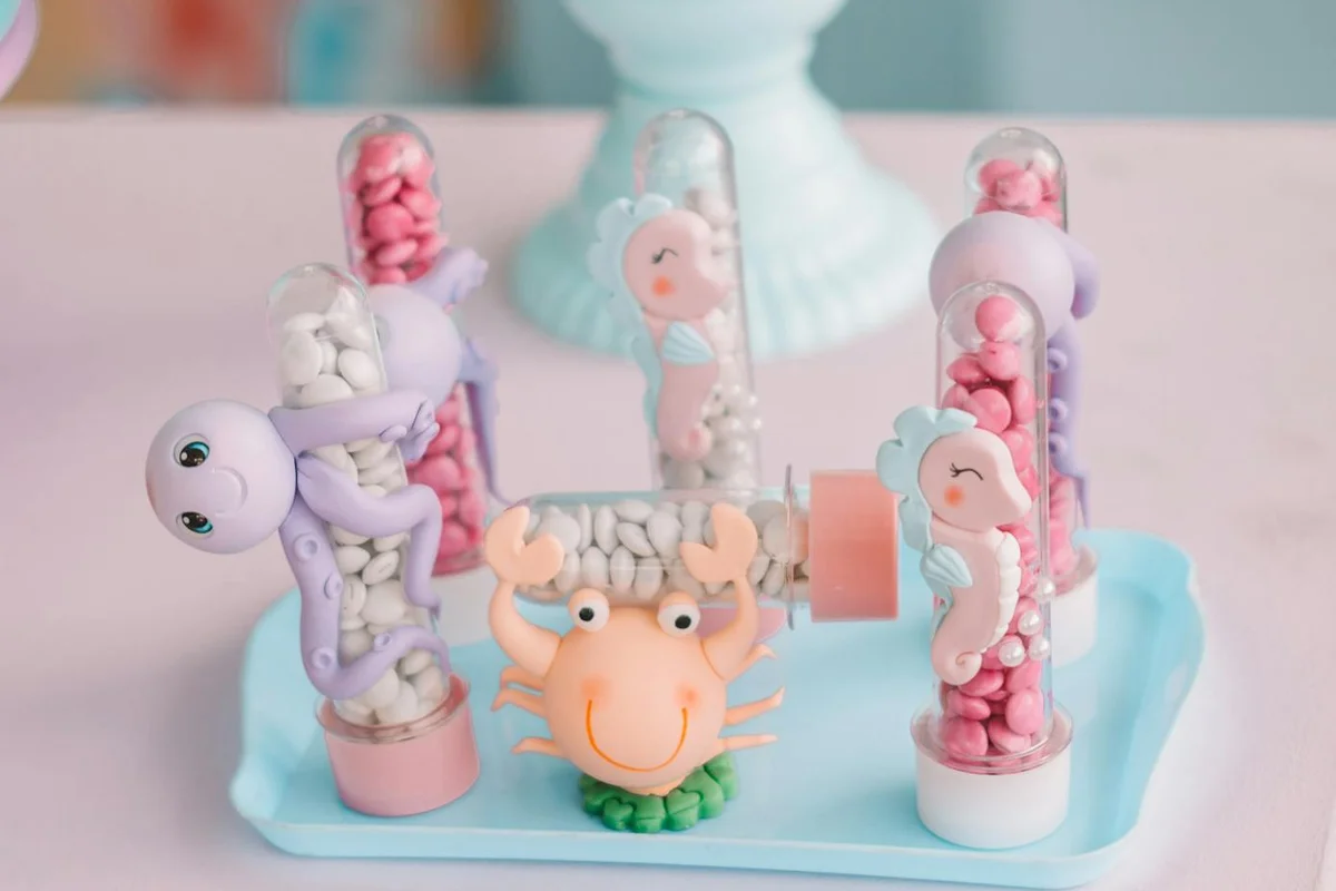 Decorative display of pastel-colored toy hermit crabs inside glass test tubes arranged on a light blue tray