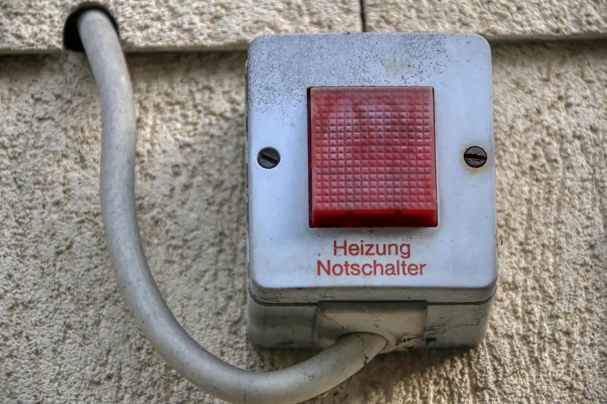 Wall-mounted electrical box with a red emergency stop button on a textured beige wall; text on the device appears to read 'Heizung Notenschalter'.