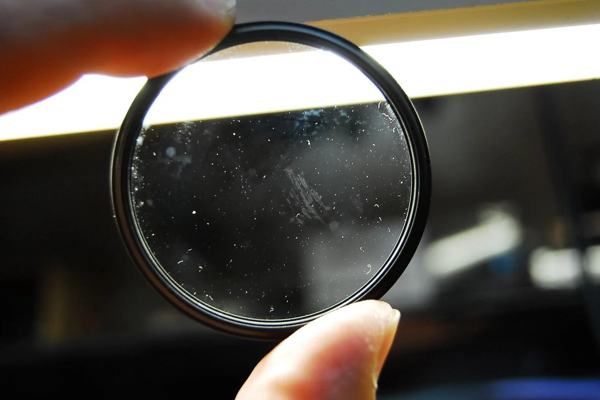 Close-up of a hand holding a circular magnifying glass to inspect a hermit crab enclosure for mold growth