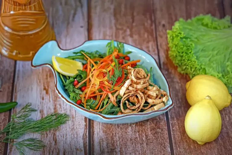 Colorful organic vegetables arranged in a shell-shaped dish on a wooden table, with lemons and dill nearby.