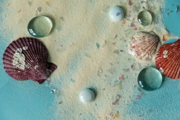 Top-down view of a variety of seashells on a pastel turquoise surface, with several shells that appear painted.
