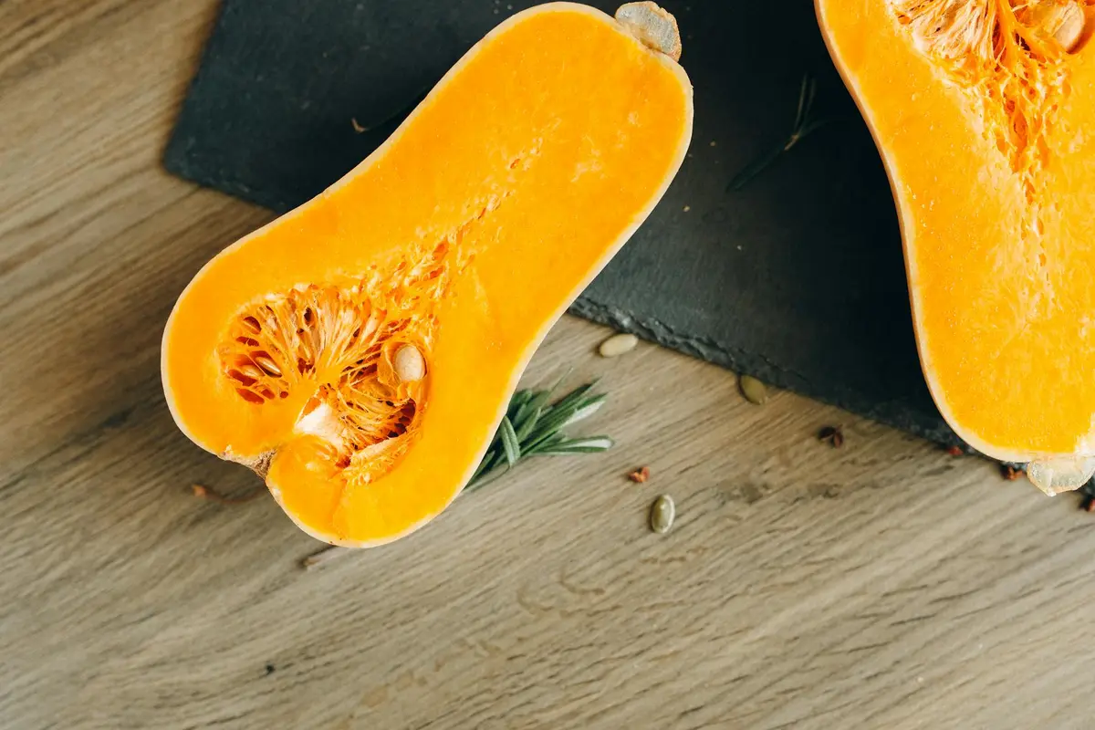 Halved orange pumpkin/squash with exposed seeds on a wooden surface